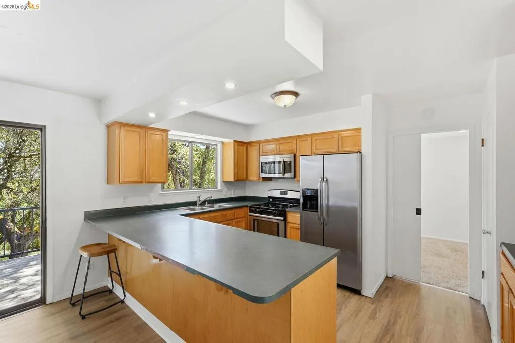 Kitchen featuring light wood cabinetry, U-shaped countertop with breakfast bar, stainless steel appliances, and wood-finish flooring