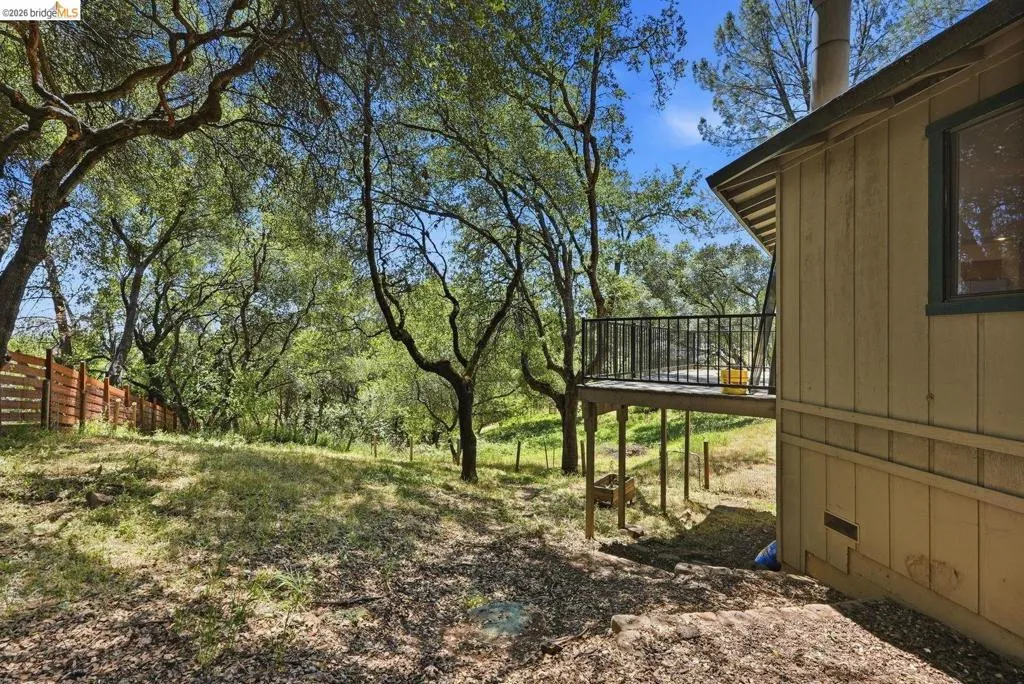 Exterior featuring a raised wood deck with black metal railing, wood siding, and surrounding mature trees