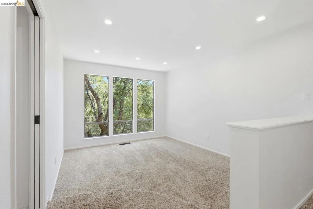 Bright room featuring three large windows, recessed lighting, neutral carpeting, and a half-wall partition