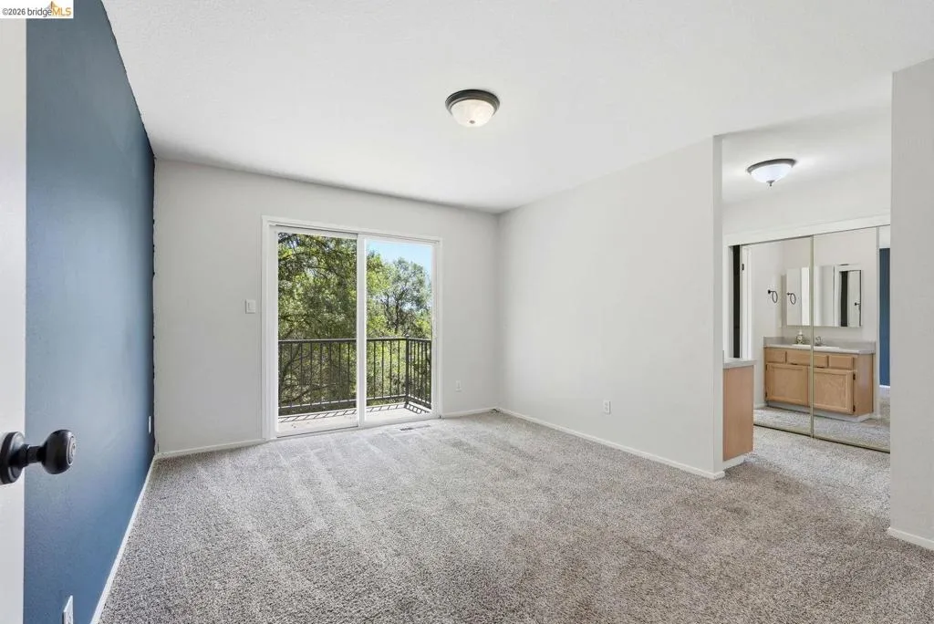 Room featuring a private balcony with black metal railings, light gray carpeting, and a blue accent wall