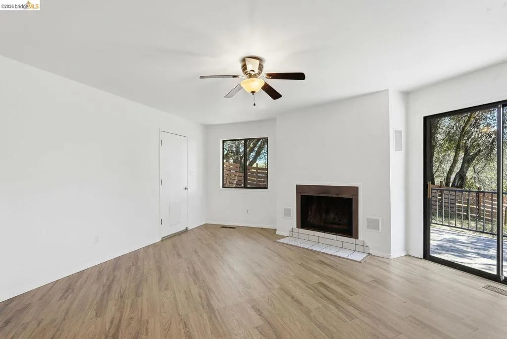 Living area featuring wood-finish flooring, a ceiling fan with integrated lighting, and a fireplace with a tile hearth