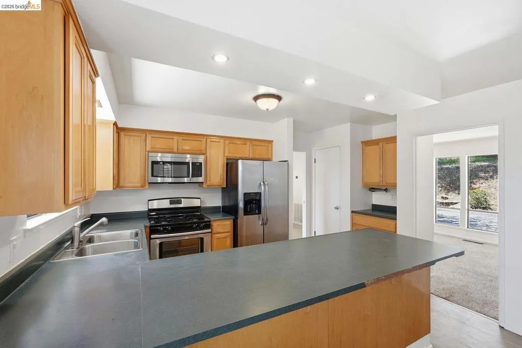 Kitchen featuring wood cabinetry, stainless steel appliances, a double basin sink, and a large breakfast bar