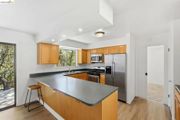 Kitchen featuring light wood cabinetry, U-shaped countertop with breakfast bar, stainless steel appliances, and wood-finish flooring