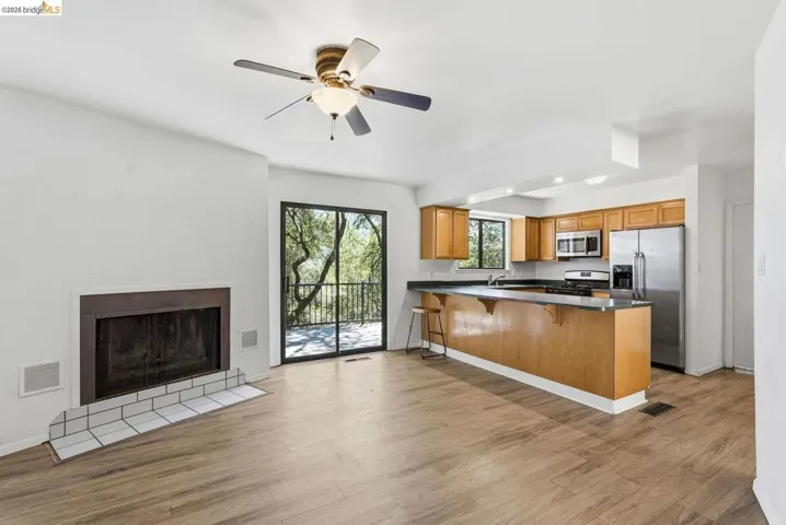 Open-concept living area featuring wood-finish flooring, a fireplace with a white tile hearth, and a ceiling fan