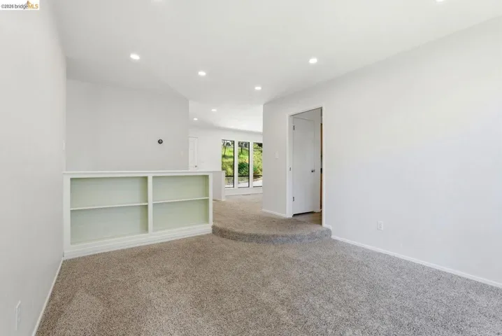 Carpeted interior space featuring a built-in white shelving unit, recessed lighting, and white walls