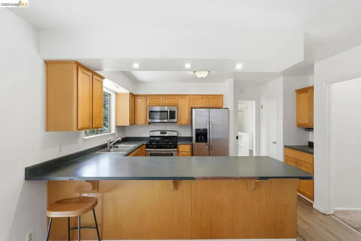 Kitchen featuring wood cabinetry, stainless steel appliances, dark countertops, and a peninsula with bar seating
