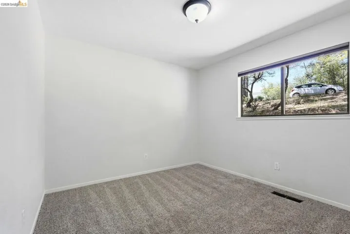 Carpeted interior room featuring a window with natural light, white walls, and a ceiling-mounted light fixture