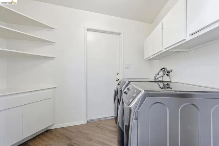 Laundry area featuring wood-finish flooring, white built-in shelving, white overhead cabinetry, and a white built-in lower cabinet