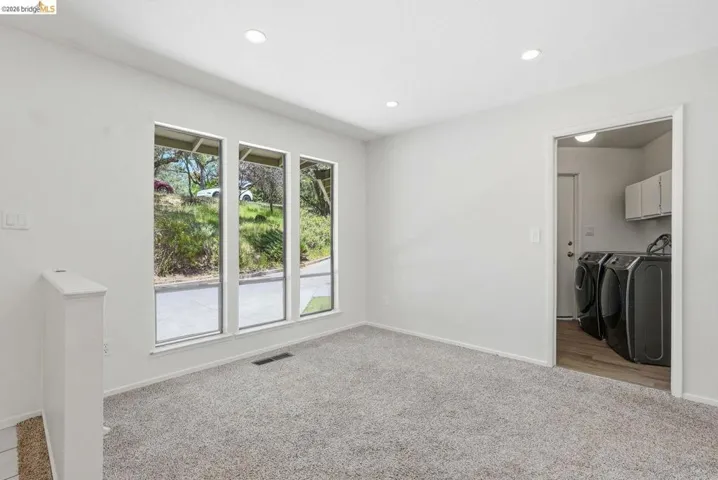 Bright room featuring three large windows, recessed ceiling lighting, light-colored carpeting, and a dedicated laundry room entrance with wood-finish flooring