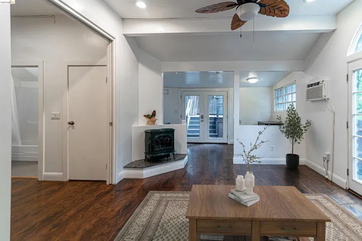 Living space featuring rich wood-finish flooring, a decorative corner stove with a stone hearth, and a ceiling fan with leaf-shaped blades