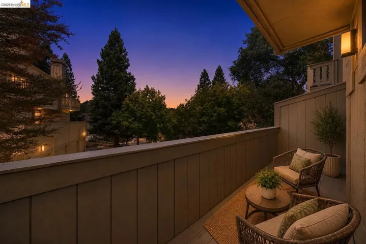Private balcony with plank flooring, a solid railing, and architectural wall sconces