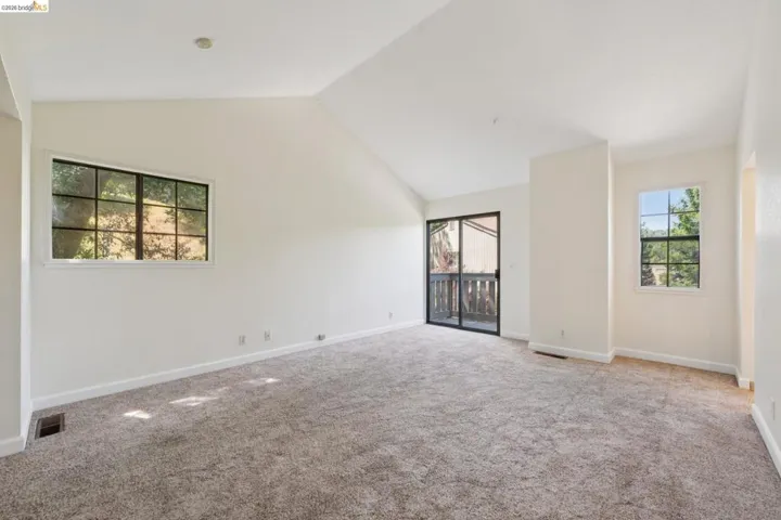 Spacious room featuring vaulted ceilings, plush carpet flooring, and multiple windows