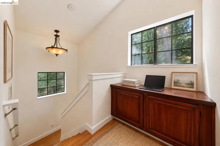 Upper landing featuring a built-in wood-finish cabinet with panel doors, a large transom window with black muntins, a smaller rectangular window, and a ceiling-mounted light fixture