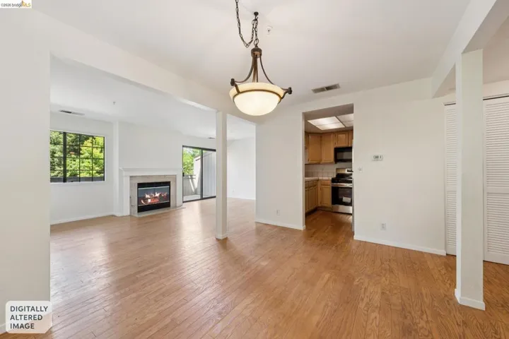 Bright living space featuring wood-finish flooring, a contemporary fireplace with a light-toned surround, and a large window with exterior​​‌​​​​‌​​‌‌​​‌​​​‌‌​​​‌​​‌‌​​‌‌​​‌‌​​​​ greenery