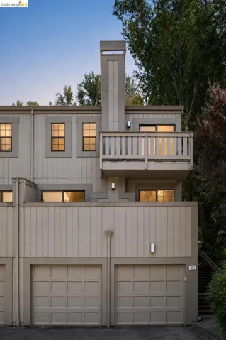 Multi-level exterior featuring a private balcony with wood railing, two single-car garages, and recessed windows