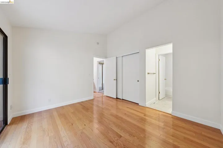 Spacious interior room featuring wood-finish flooring, white walls, and high ceilings