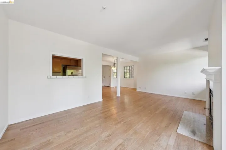 Spacious interior featuring wood-finish flooring, a white-tiled fireplace with a classic mantel, and a pass-through window with a tiled bar-height counter