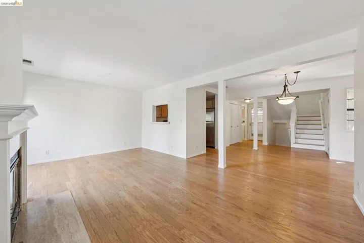 Expansive living area featuring wood-finish flooring, a white mantel fireplace with a stone hearth, and a pass-through window with wood cabinetry