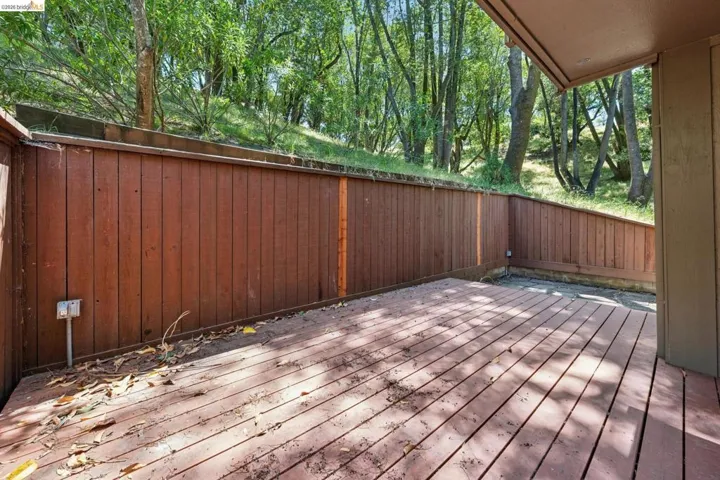Spacious outdoor deck featuring natural wood decking, a solid wood privacy fence, and a wooded hillside backdrop