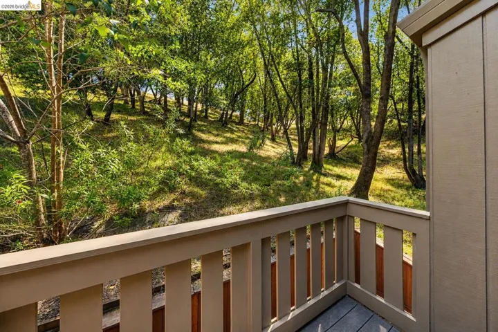 Outdoor balcony featuring a composite deck and a light-colored railing, overlooking a wooded hillside with mature trees and ground cover