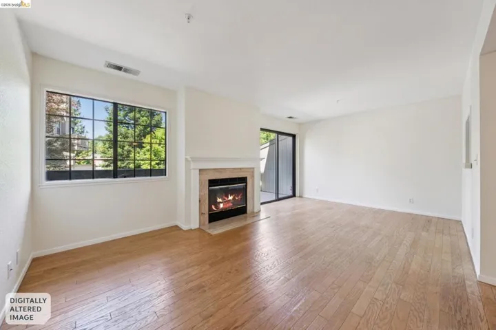 Spacious interior featuring wood-finish flooring, a contemporary fireplace with a stone surround and white mantel, a large window with black gridding, a sliding glass door, and neutral-toned walls