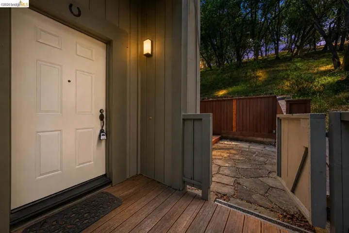 Front entry featuring a solid paneled door, wood-finish decking, and a wall-mounted exterior light fixture