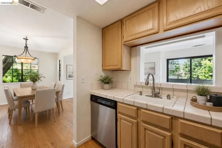Kitchen featuring light wood cabinetry, white tile countertops, and a stainless steel dishwasher