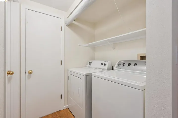 Dedicated laundry space featuring a white washer and dryer, a wall-mounted shelving unit, and wood-finish flooring