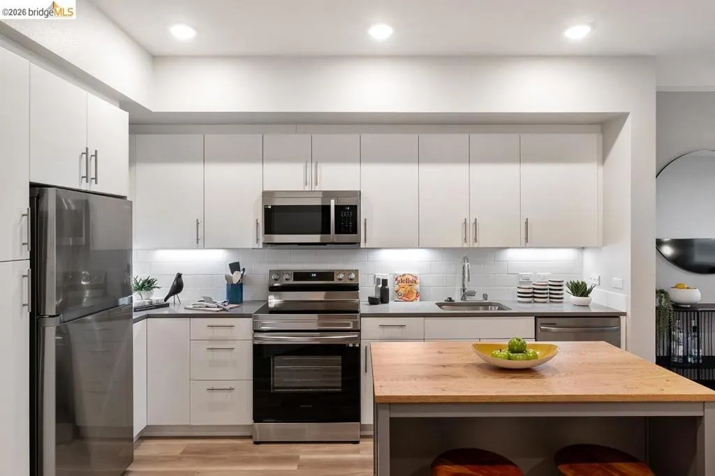 Kitchen with wooden counters, stainless steel appliances, decorative backsplash, white cabinetry, and light wood-style flooring