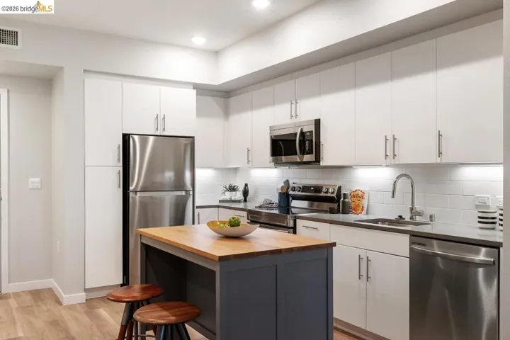 Kitchen with decorative backsplash, stainless steel appliances, butcher block counters, white cabinetry, and light wood-style flooring