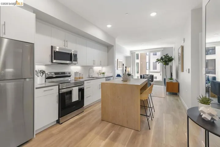 Modern kitchen featuring a light wood-finish island, white flat-panel cabinetry, stainless steel appliances, and wood-finish flooring