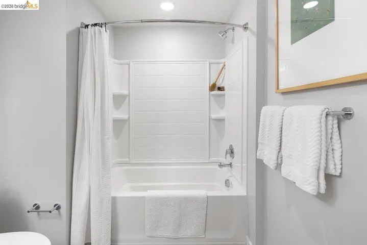 White tub-shower combination unit featuring integrated shelving, chrome fixtures, and a curved shower rod