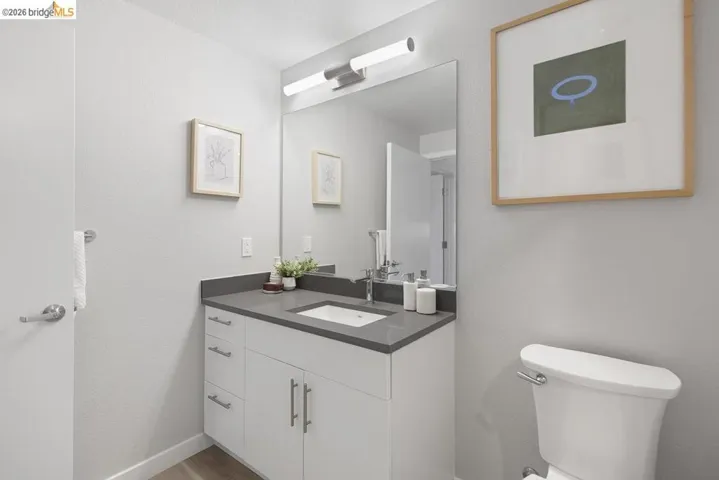 Bathroom featuring a white vanity with a gray countertop, an integrated sink with chrome fixtures, a large wall-mounted mirror, and wood-finish flooring