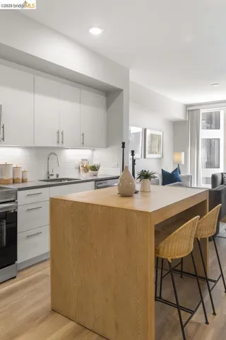 Open-concept kitchen featuring light wood-finish flooring, white cabinetry with brushed nickel hardware, a subway tile backsplash, and recessed lighting