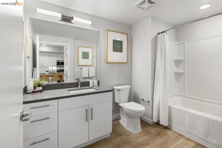 Bathroom featuring a spacious vanity with an undermount sink and gray countertop, wood-finish flooring, a white toilet, and a bathtub with a shower and white subway tile surround