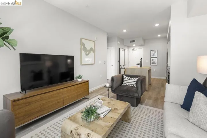 Open-concept living area featuring light-toned walls, recessed lighting, wood-finish flooring, a contemporary island, and a built-in media console