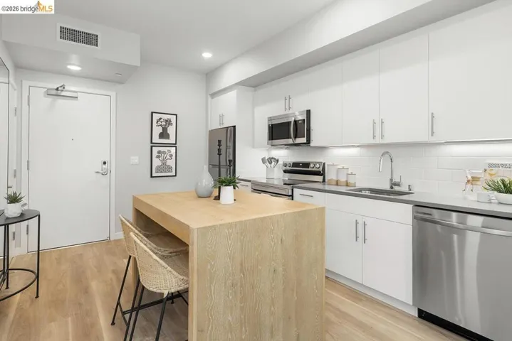 Contemporary kitchen featuring stainless steel appliances, white flat-panel cabinetry, white subway tile backsplash, and a light wood-finish island with seating