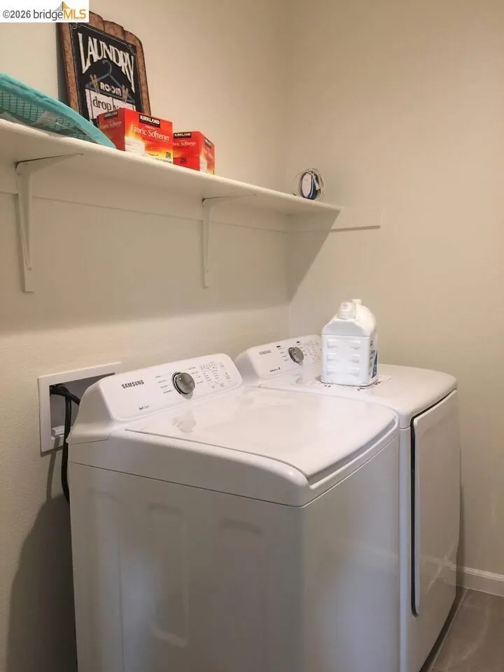 Dedicated laundry area featuring white top-load appliances and a wall-mounted shelving unit