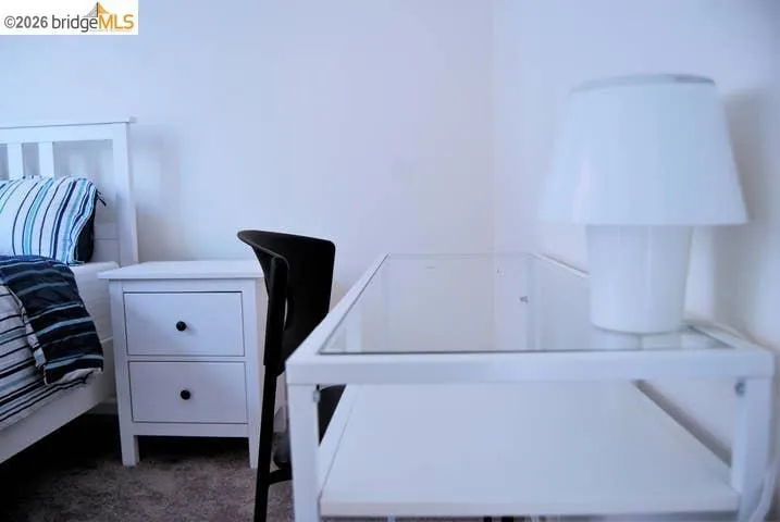 White nightstand with two drawers and black pulls, paired with a white-framed bed