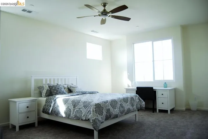 Spacious room featuring a ceiling fan, a large window, a smaller upper window, and light-colored walls