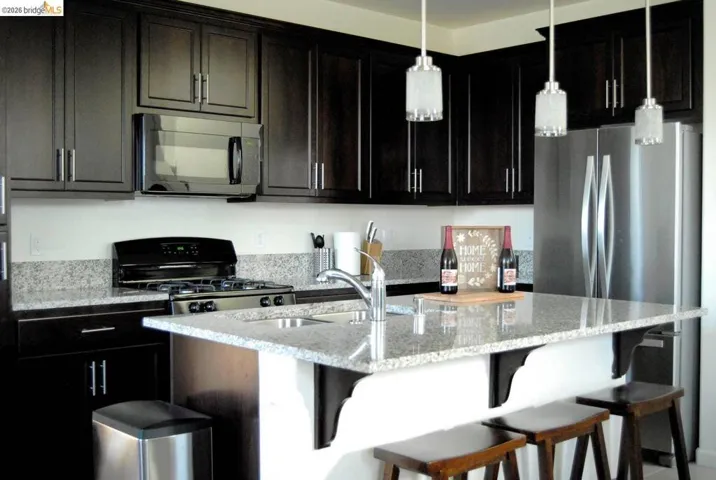 Kitchen featuring dark wood cabinetry with brushed nickel hardware, light granite countertops, and stainless steel appliances