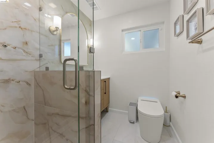 Shower enclosure featuring glass panels and marble-look tile surround