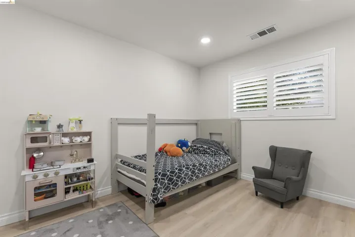 Spacious room featuring light wood-finish flooring, recessed lighting, white baseboards, and a window with white plantation shutters