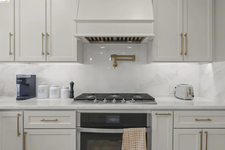 Integrated cooktop with a wall-mounted pot filler, under-cabinet lighting, and a custom range hood