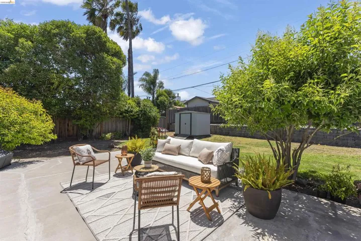 Expansive concrete patio with a lush lawn, mature trees, wood fencing, and a storage shed