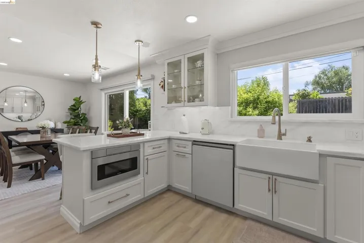 Kitchen featuring a white farmhouse sink, stainless steel appliances, white cabinetry, quartz countertops, and a full-height tile backsplash