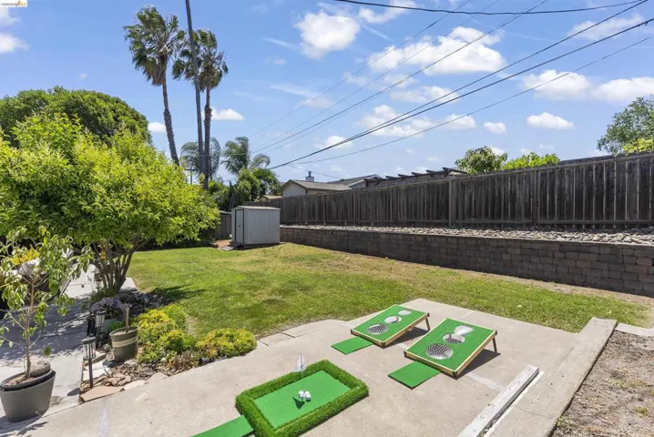 Expansive backyard featuring a green lawn, mature trees, concrete patio, a retaining wall, and a wood fence