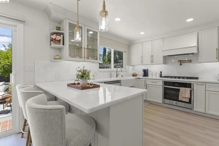 Modern kitchen featuring light gray cabinetry, a central island with countertop seating, white stone countertops, and wood-finish flooring