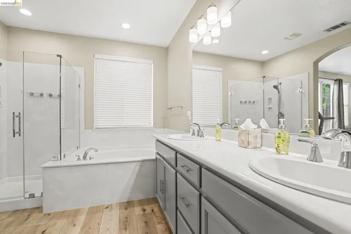 Bathroom featuring wood-finish flooring, a double vanity with undermount sinks, a built-in tub, and a glass-enclosed shower