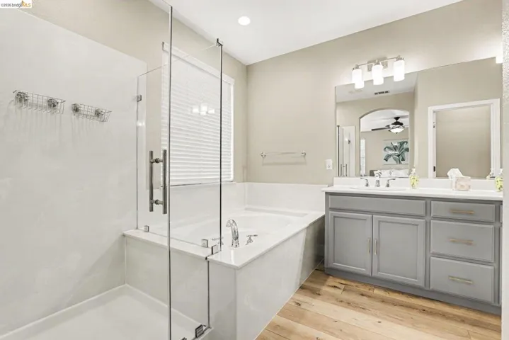 Contemporary bathroom featuring a glass-enclosed shower, a deep soaking tub, and a dual-sink vanity with gray cabinetry